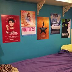 a bed with purple sheets and posters on the wall above it in a blue room