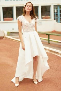 a woman is standing in front of a building wearing a white dress with lace on it