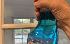 a hand is holding a bottle of detergent in front of a window sill