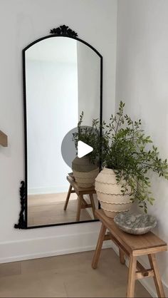 a mirror sitting on top of a wooden table next to a vase filled with plants