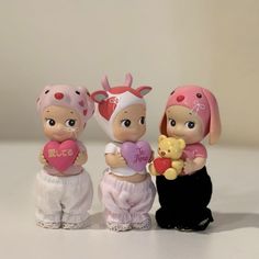 three small figurines are sitting on a table with one holding a heart and the other holding a teddy bear