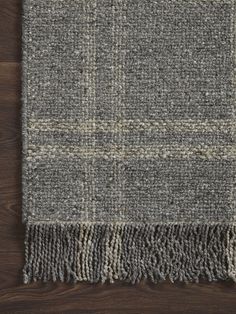 a gray and white rug with fringes on top of a wooden floor next to a wall