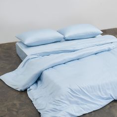 an unmade bed with light blue sheets and pillow cases on top of the bed