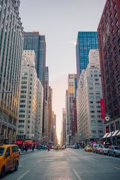 an empty city street with tall buildings in the back ground and cars parked on the side