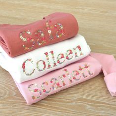 three pink and white shirts with sequins on them sitting on top of a wooden table