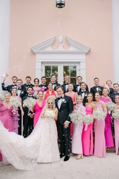 a large group of people standing in front of a building with pink dresses and tuxedos