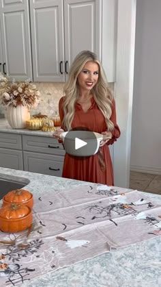 a woman standing in front of a kitchen counter holding an orange and white plate with pumpkins on it