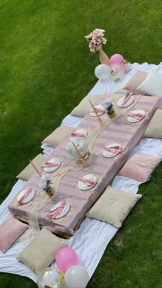 a table set up with pink and white desserts on top of it in the grass