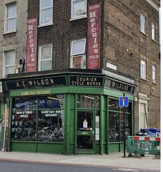 a green store front sitting on the side of a road next to tall brick buildings