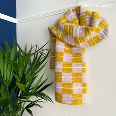 a yellow and white scarf hanging on a wall next to a potted green plant