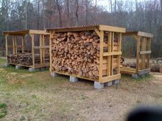 several large piles of wood stacked on top of each other in front of some trees