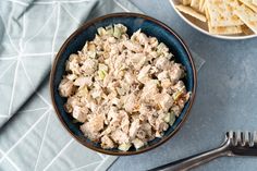 a blue bowl filled with chicken salad next to crackers and a fork on a table