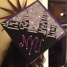 a woman wearing a graduation cap decorated with purple and white beads, the word w is written on it