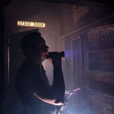 a man standing in front of a stage door drinking from a wine glass at night