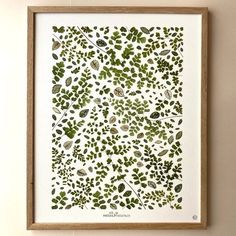 an art print with green leaves on white paper in a wooden frame hanging on the wall