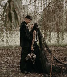 a man and woman dressed up in black standing next to each other under a tree