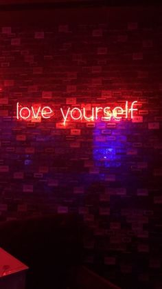 a neon sign that says love yourself on a brick wall