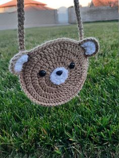 a crocheted teddy bear hanging from a string on the grass in front of a fence