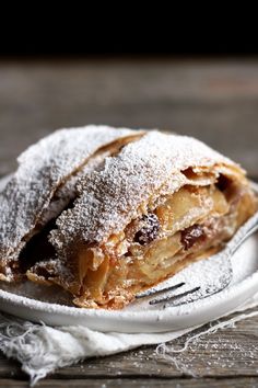 a piece of pie on a plate with a fork in the foreground and powdered sugar on top