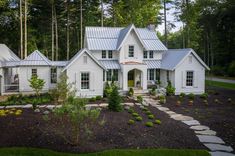 a large white house surrounded by trees in the middle of a forest with stone walkways