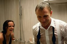 a man with suspenders and a tie is looking at his cell phone in the bathroom