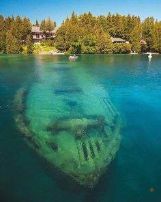 an underwater view of a boat wreck in the water with trees and houses in the background