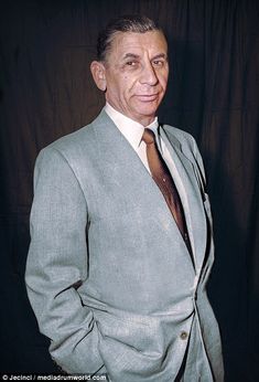 a man in a gray suit and tie posing for a photo with his hands in his pockets