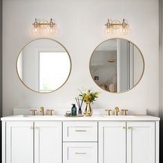 two round mirrors on the wall in a bathroom with white cabinets and gold trimmings