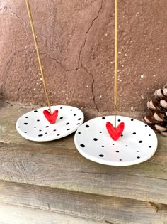 two plates with red hearts on them are sitting next to pine cones and one has a stick in the shape of a heart