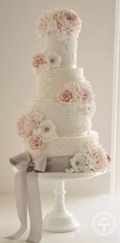 a three tiered wedding cake with pink flowers and ribbons on the top, sitting on a white pedestal