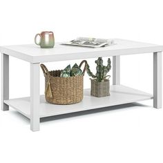 a white coffee table with two plants and a basket on the bottom, next to a newspaper rack