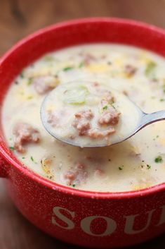 a red bowl filled with soup on top of a wooden table next to a spoon