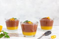 three desserts in small glass bowls on a marble surface with flowers and spoon next to them