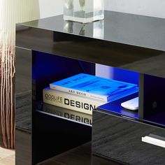 a black table with some books and a lamp on it's side stand in front of a white vase