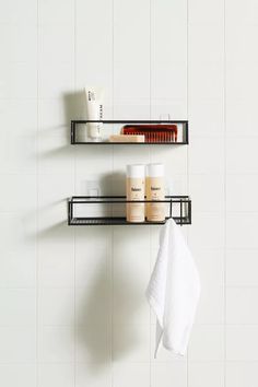 two black shelves with white towels and other bathroom items on them, against a white tiled wall