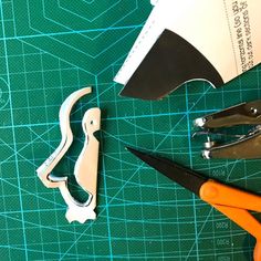 scissors, pliers and paper cutters on a green cutting mat with blue lines