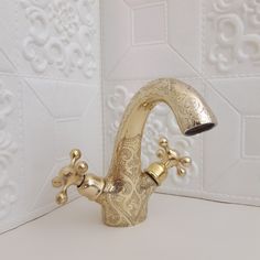 a gold faucet on a white counter in front of a wallpapered background