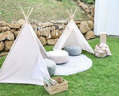 two teepee tents sitting on top of a lush green field next to a stone wall