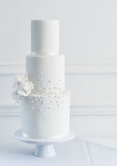 a three tiered white wedding cake with flowers on the side and pearls on the top