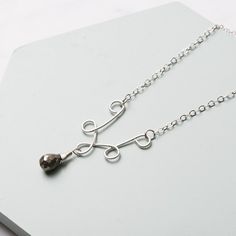 a silver necklace with a heart shaped pendant hanging from it's side on a white surface