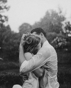 a man and woman kissing in the rain with their hands on their heads as they sit under an umbrella