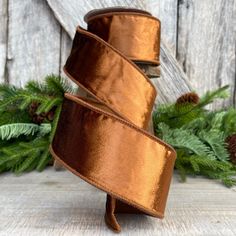 a close up of a ribbon on a wooden surface with pine cones and evergreen branches