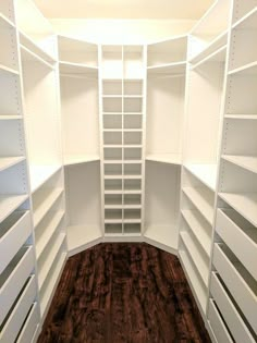 an empty walk in closet with white shelving and wood flooring on the side