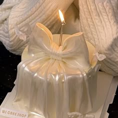 a white cake sitting on top of a table with a lit candle in the middle