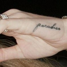 a woman with a small tattoo on her left hand and the word paradise written in cursive font