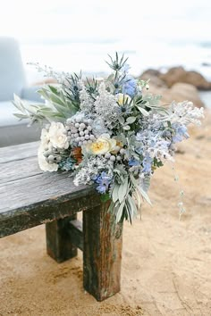 a bouquet of flowers sitting on top of a wooden bench next to the ocean and sand