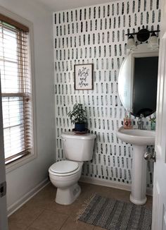 a white toilet sitting next to a bathroom sink under a mirror on top of a wall