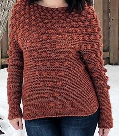 a woman standing in the snow wearing an orange sweater with crocheted flowers on it