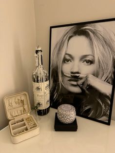 a photograph of a woman next to an empty bottle and jewelry box on a table