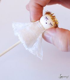 a hand holding a small white doll on a stick